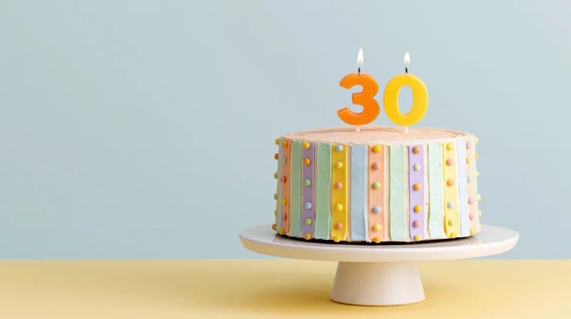 Decorated birthday cake with number thirty candles on white pedestal stand