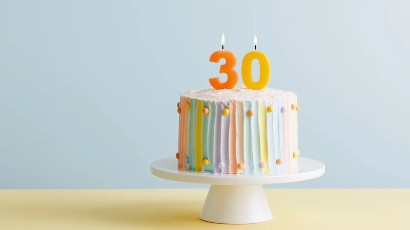 Decorated birthday cake with number thirty candles on white pedestal stand