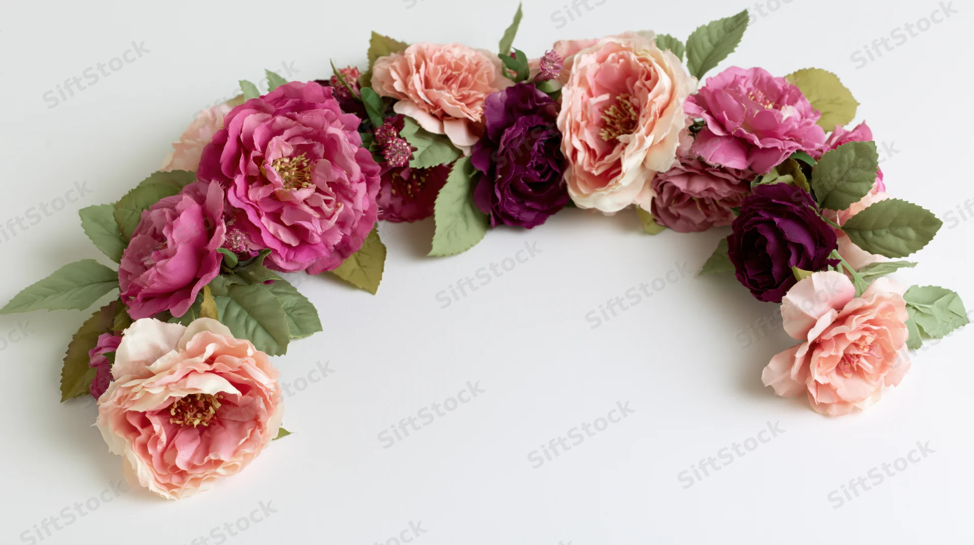 Curved floral garland with pink and purple roses and green leaves arranged in an arch on a white surface
