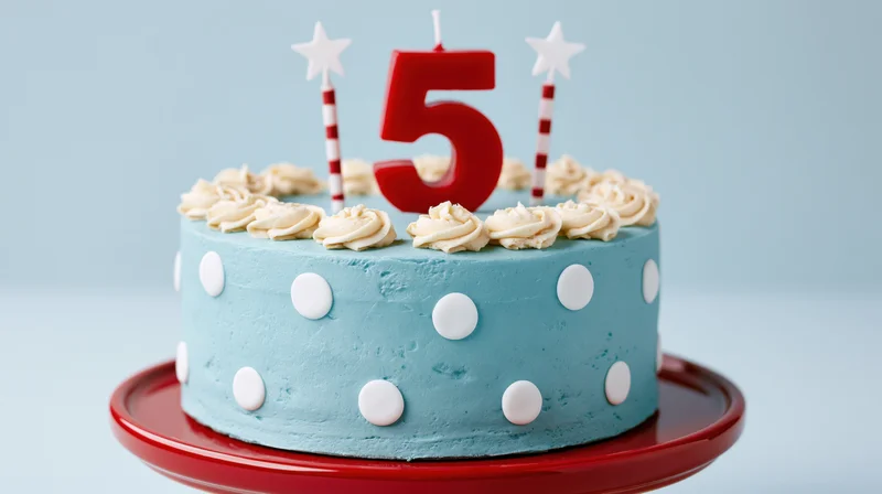 Light blue polka dot birthday cake with number five candle and star candles on red plate