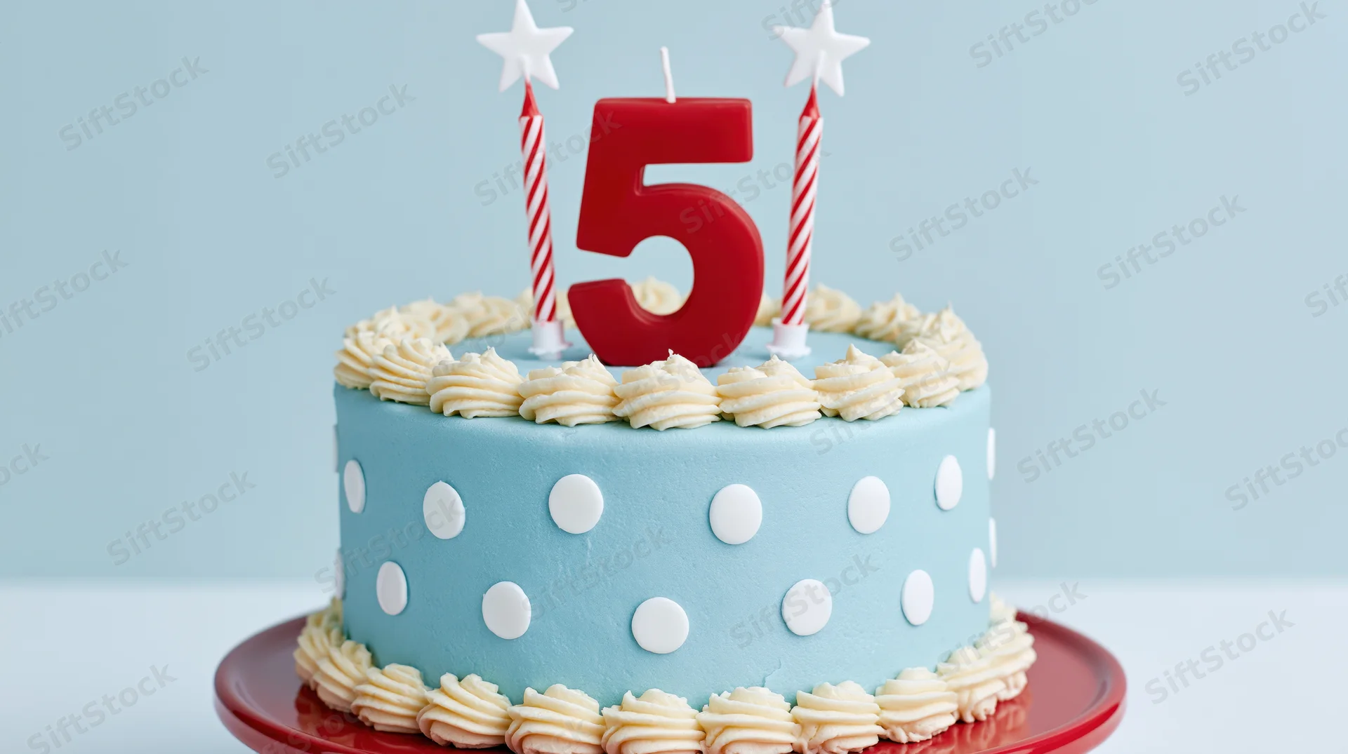 Blue polka dot birthday cake with red number five candle and star candles on red plate