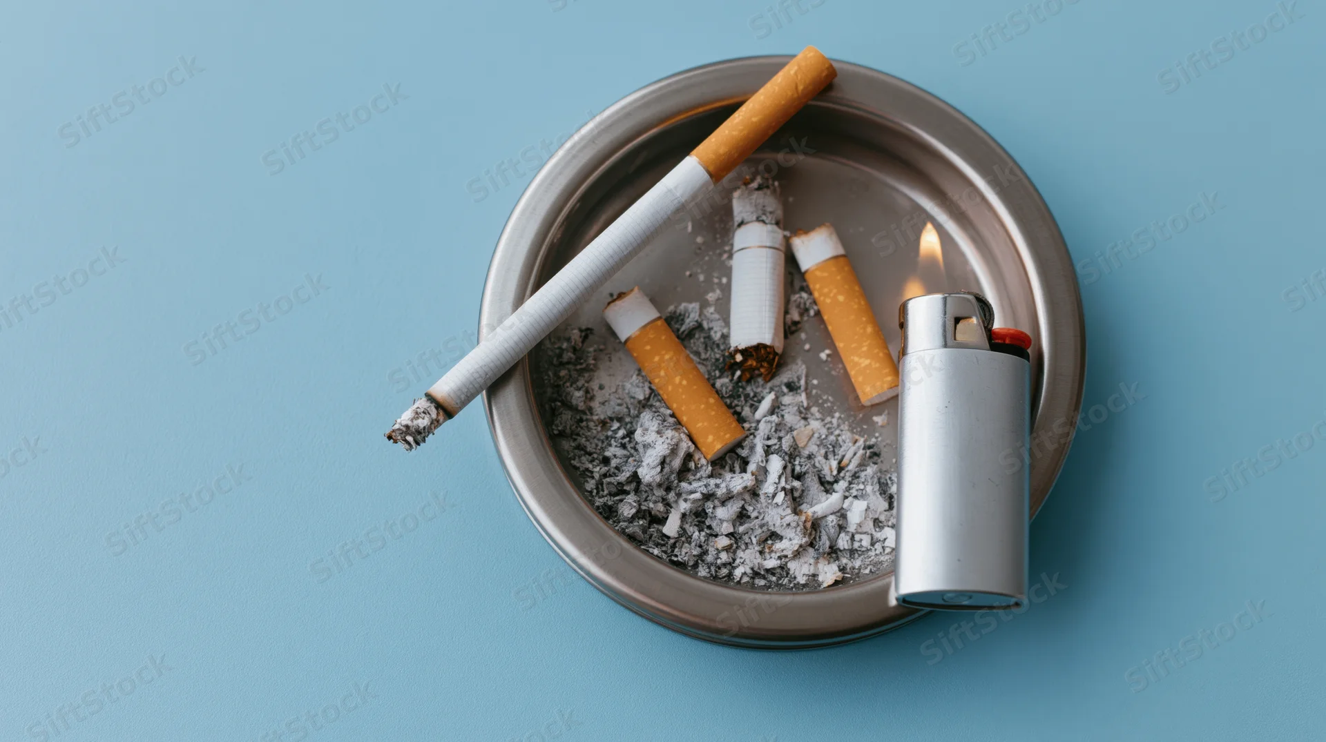 Lit cigarette resting on a metal ashtray with cigarette butts and ash, beside a lighter on a blue surface