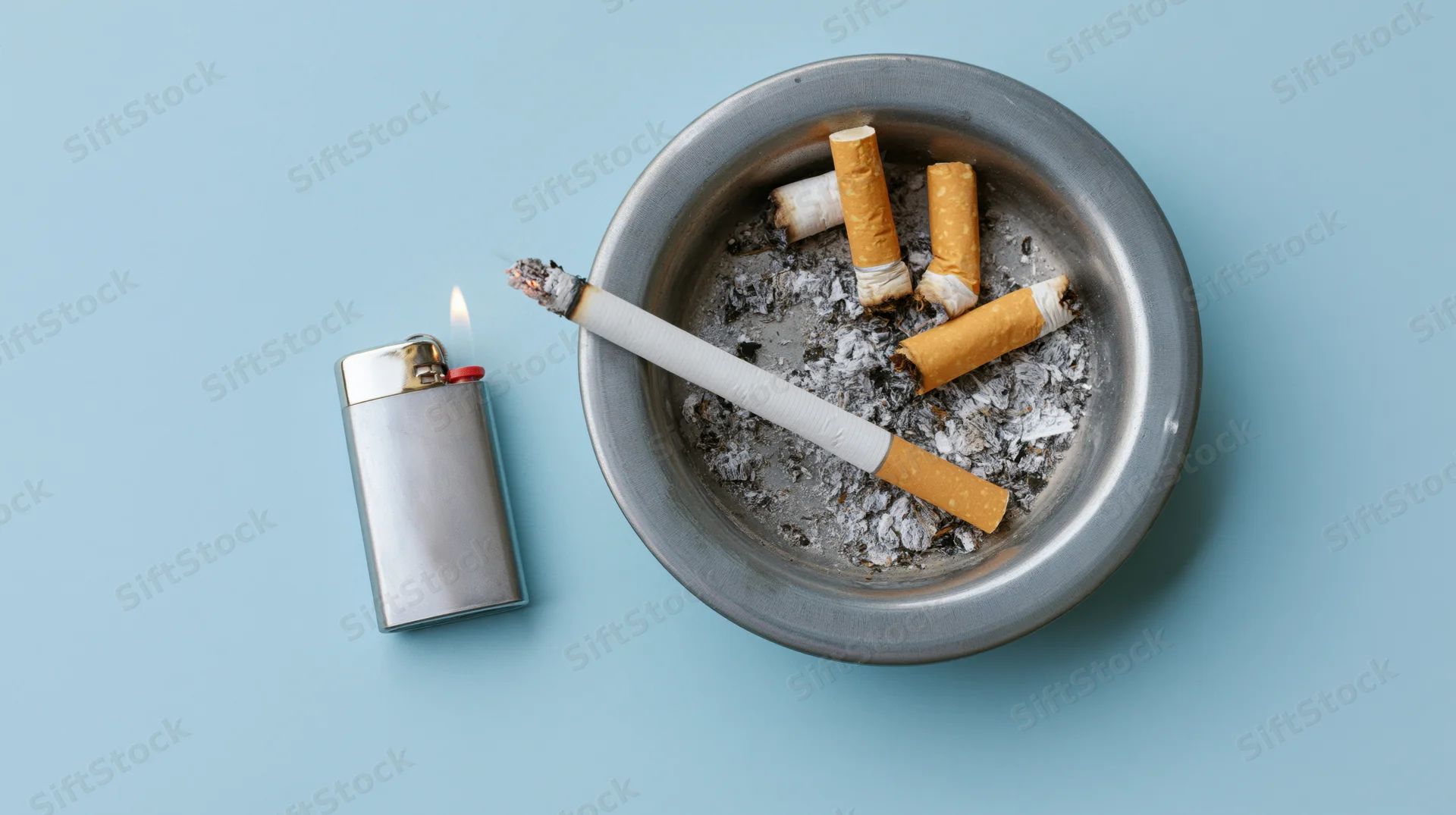 Lit cigarette resting across a metal ashtray beside a lighter on a blue surface