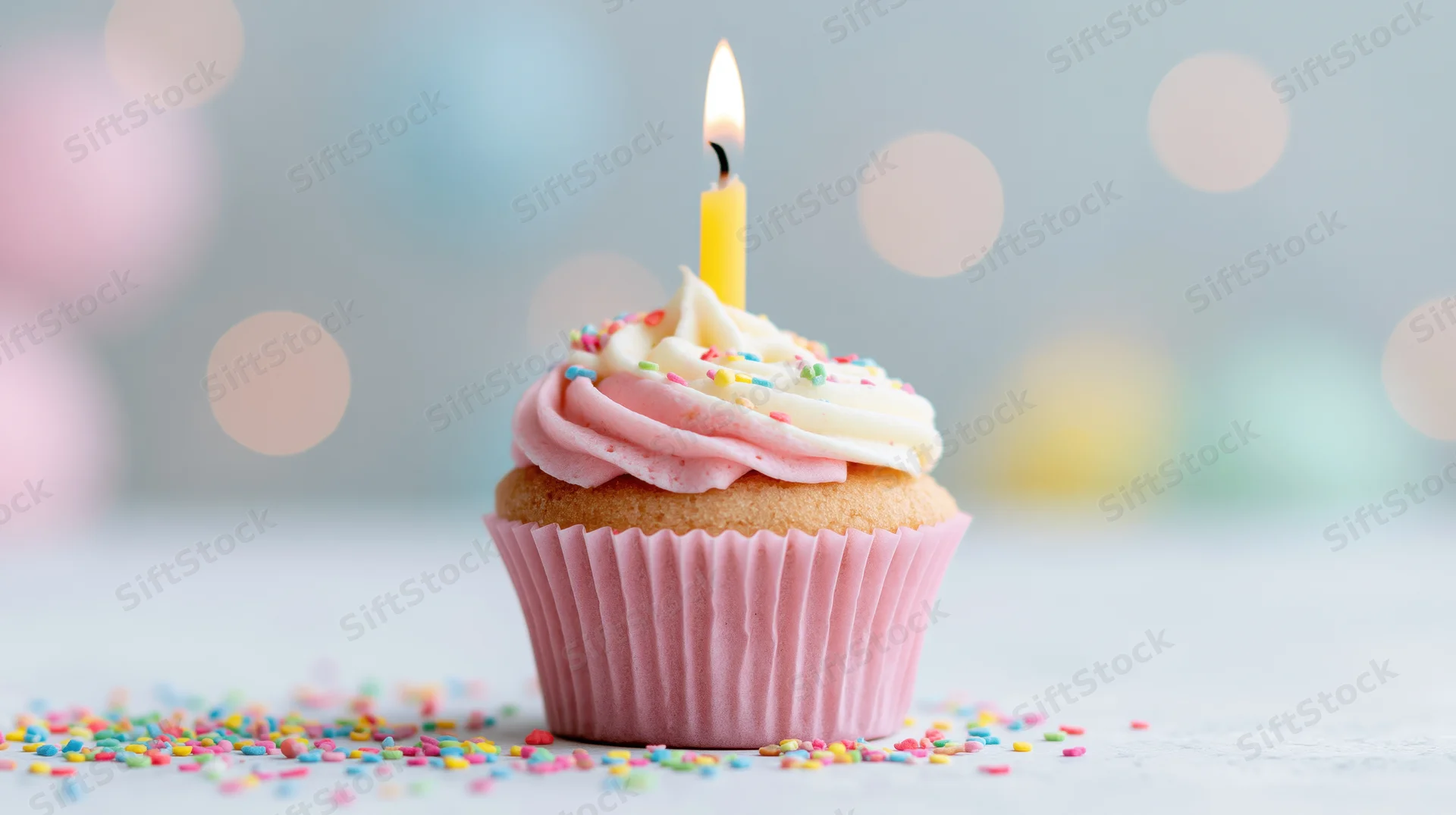 Single birthday cupcake with lit candle and sprinkles on a light surface
