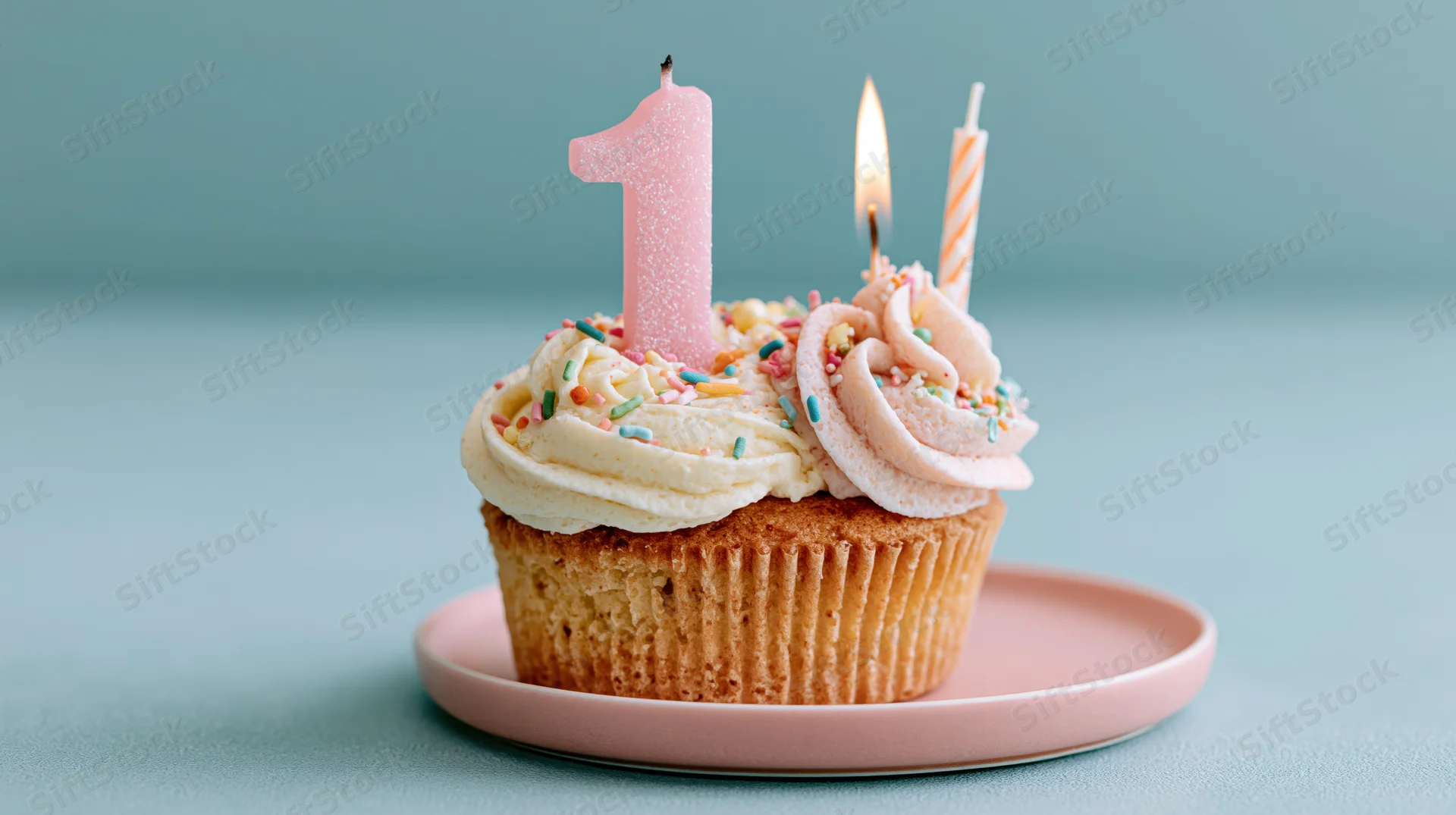 Birthday cupcake with number one candle and pastel frosting on a pink plate
