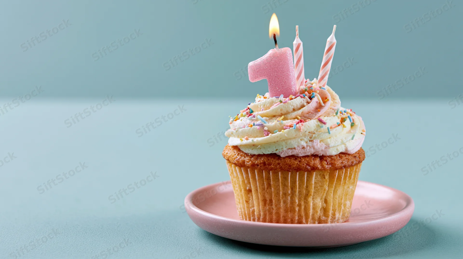 Birthday cupcake with lit number one candle and sprinkles on pink plate