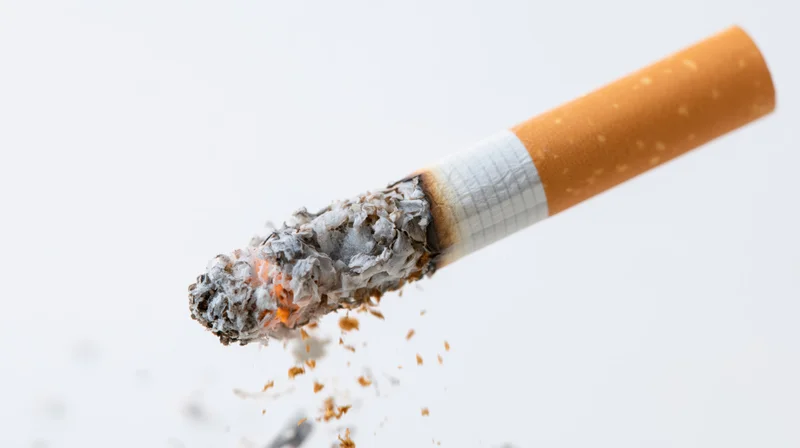 Lit cigarette burning with ash falling against white background