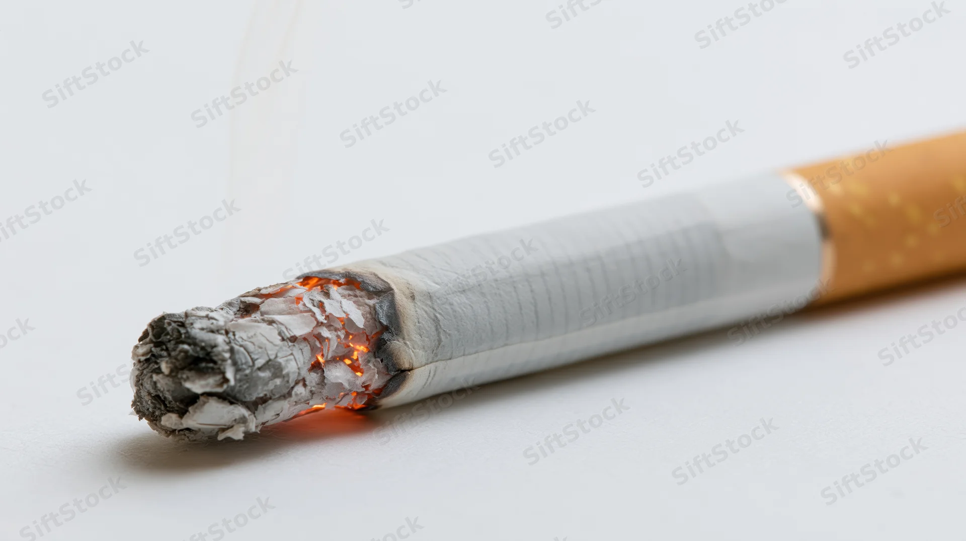 Lit cigarette burning with ash and smoke on white surface