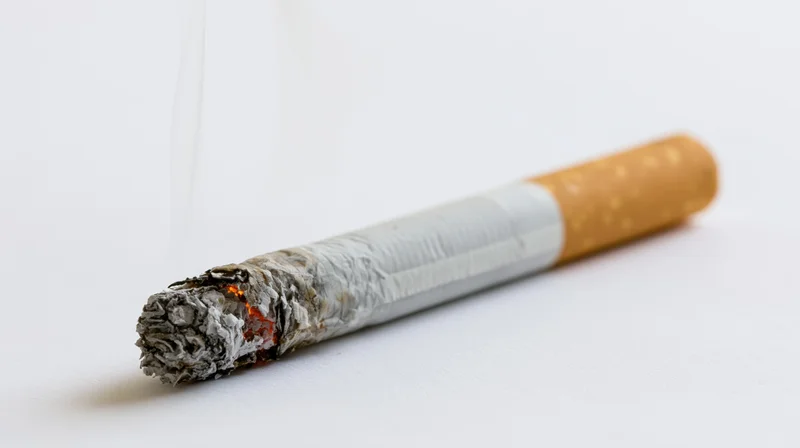 Lit cigarette with ash and smoke on white background