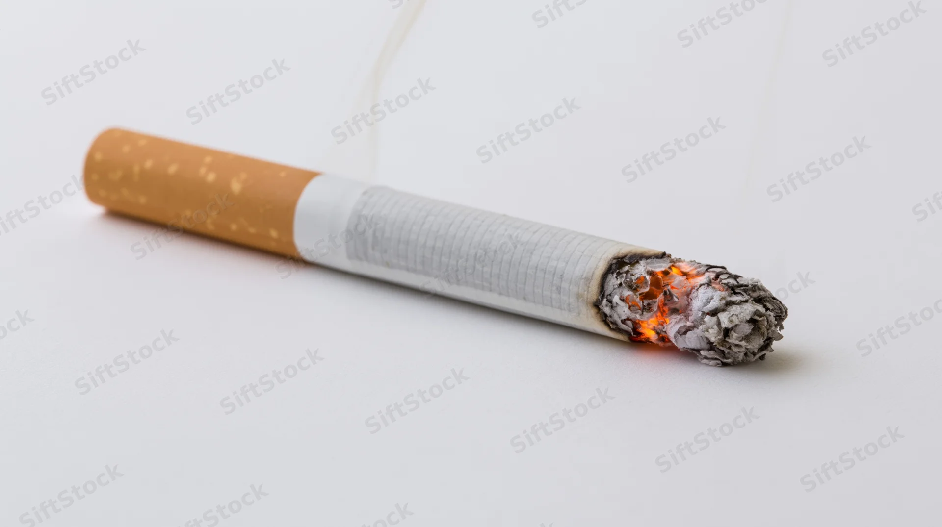 Lit cigarette burning with ash and smoke on white background