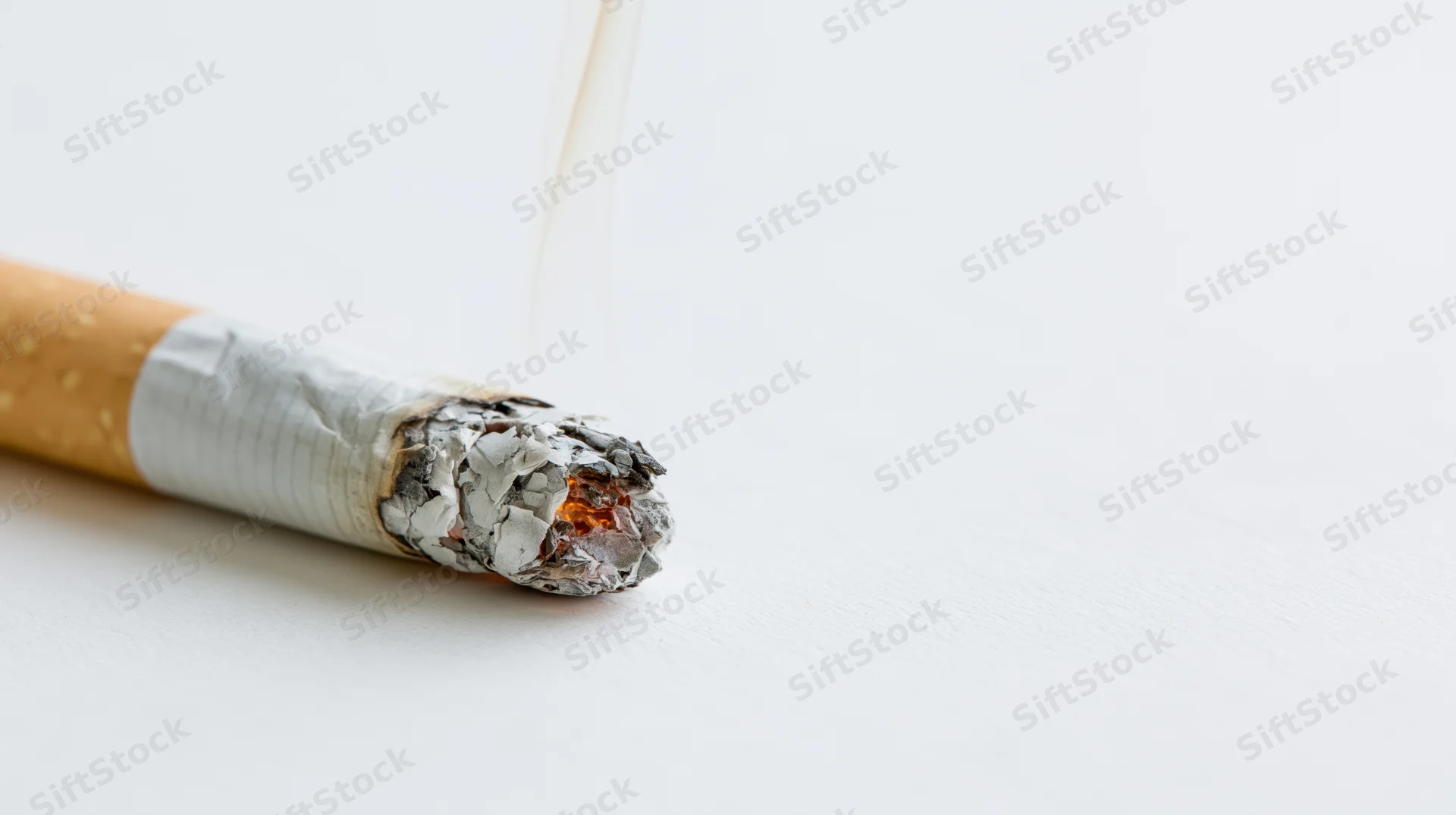 Lit cigarette with ash and smoke on white surface