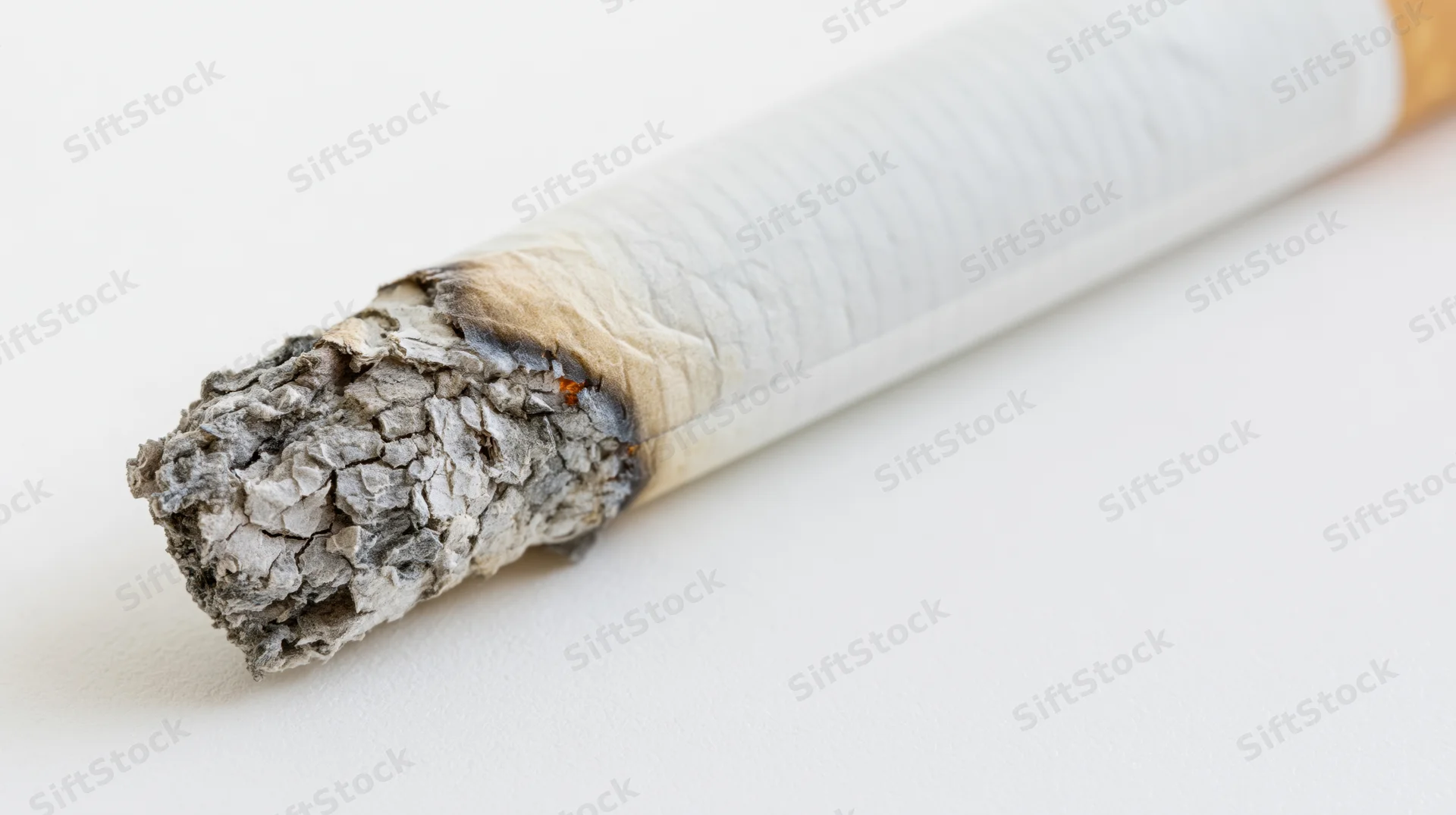 Lit cigarette with glowing ember and crumbling ash on white background