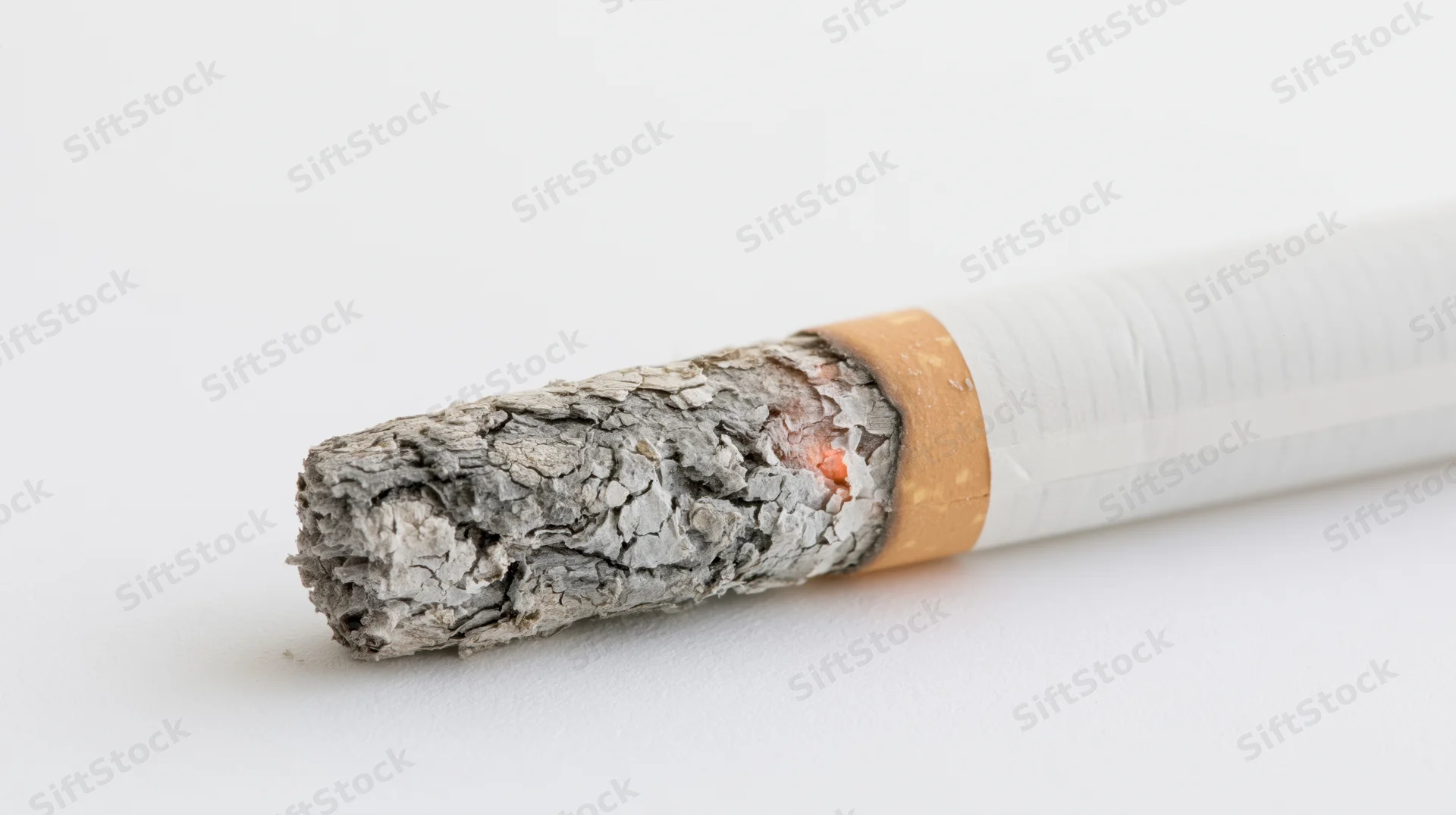 Lit cigarette with glowing ember and crumbling ash on white surface