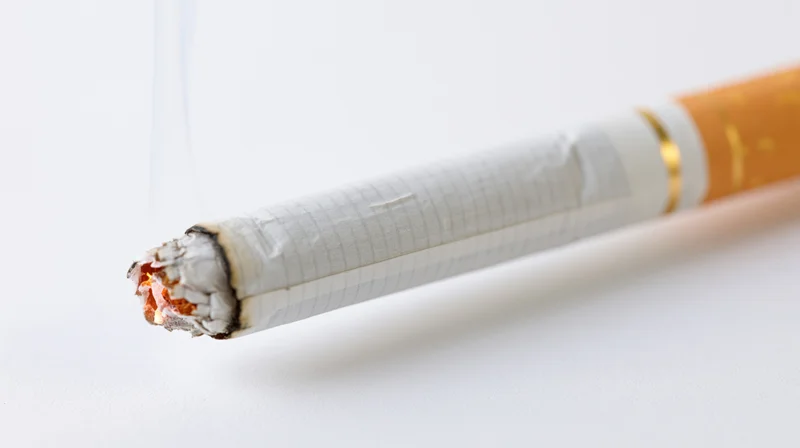 Lit cigarette with glowing ember and ash on white background