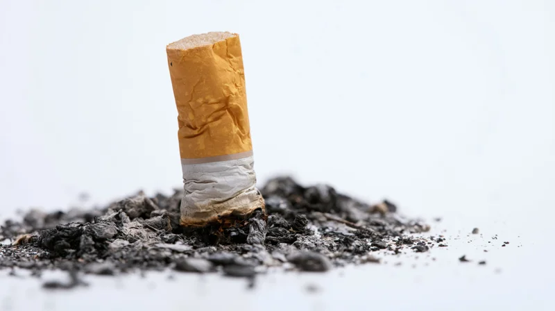 Stubbed-out cigarette butt standing upright on a pile of ash against a white background