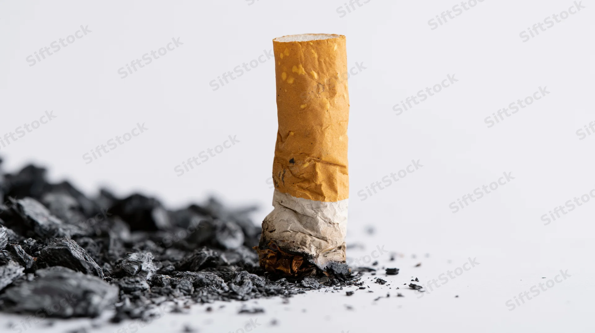Stubbed-out cigarette butt standing upright on white background surrounded by ash