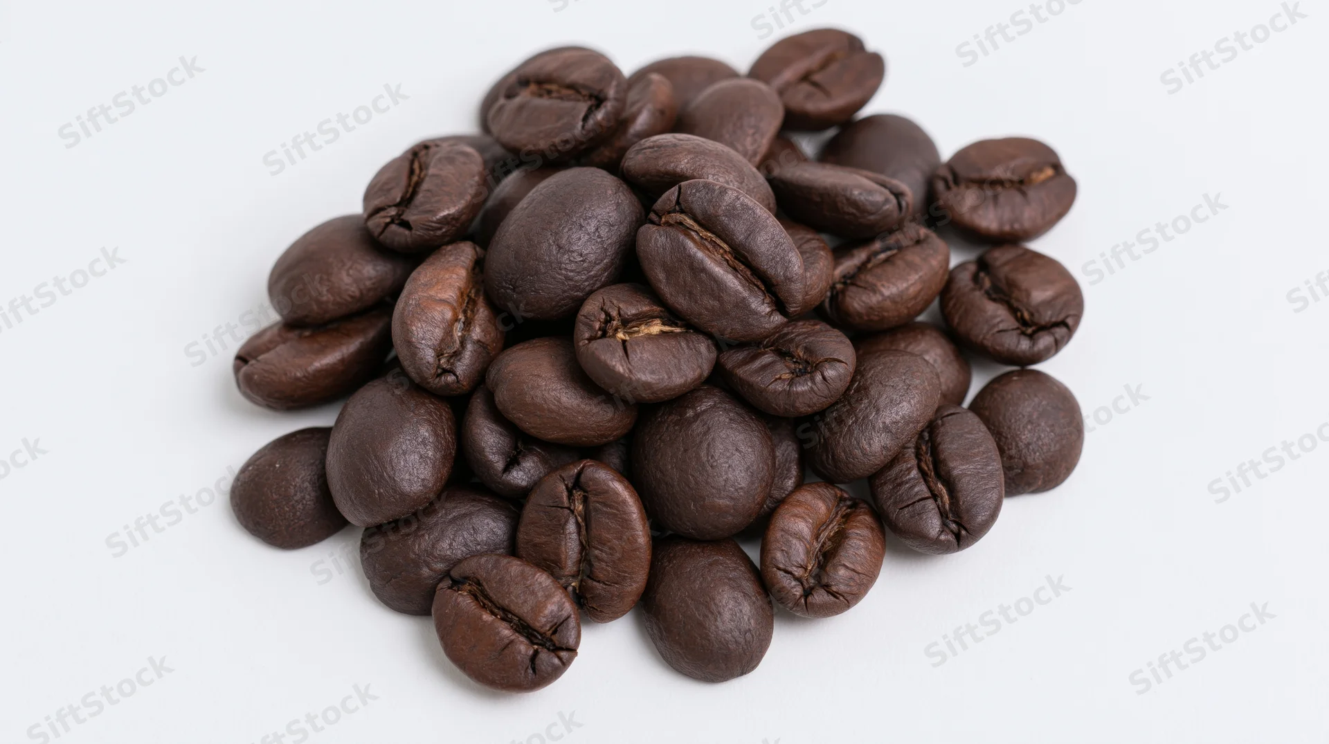 Dark roasted coffee beans piled loosely on a white surface