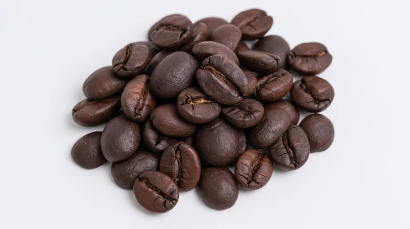 Dark roasted coffee beans piled loosely on a white surface