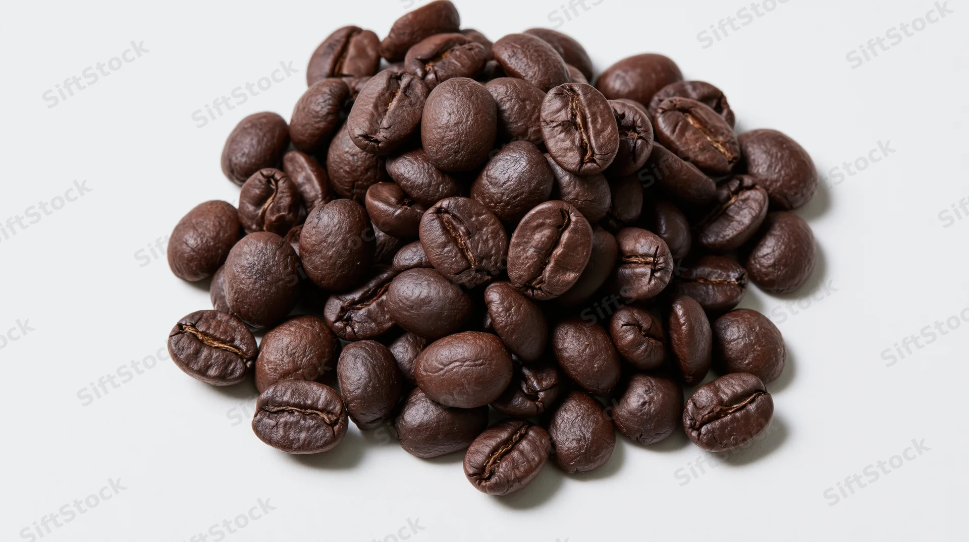 Dark roasted coffee beans piled loosely on a white surface