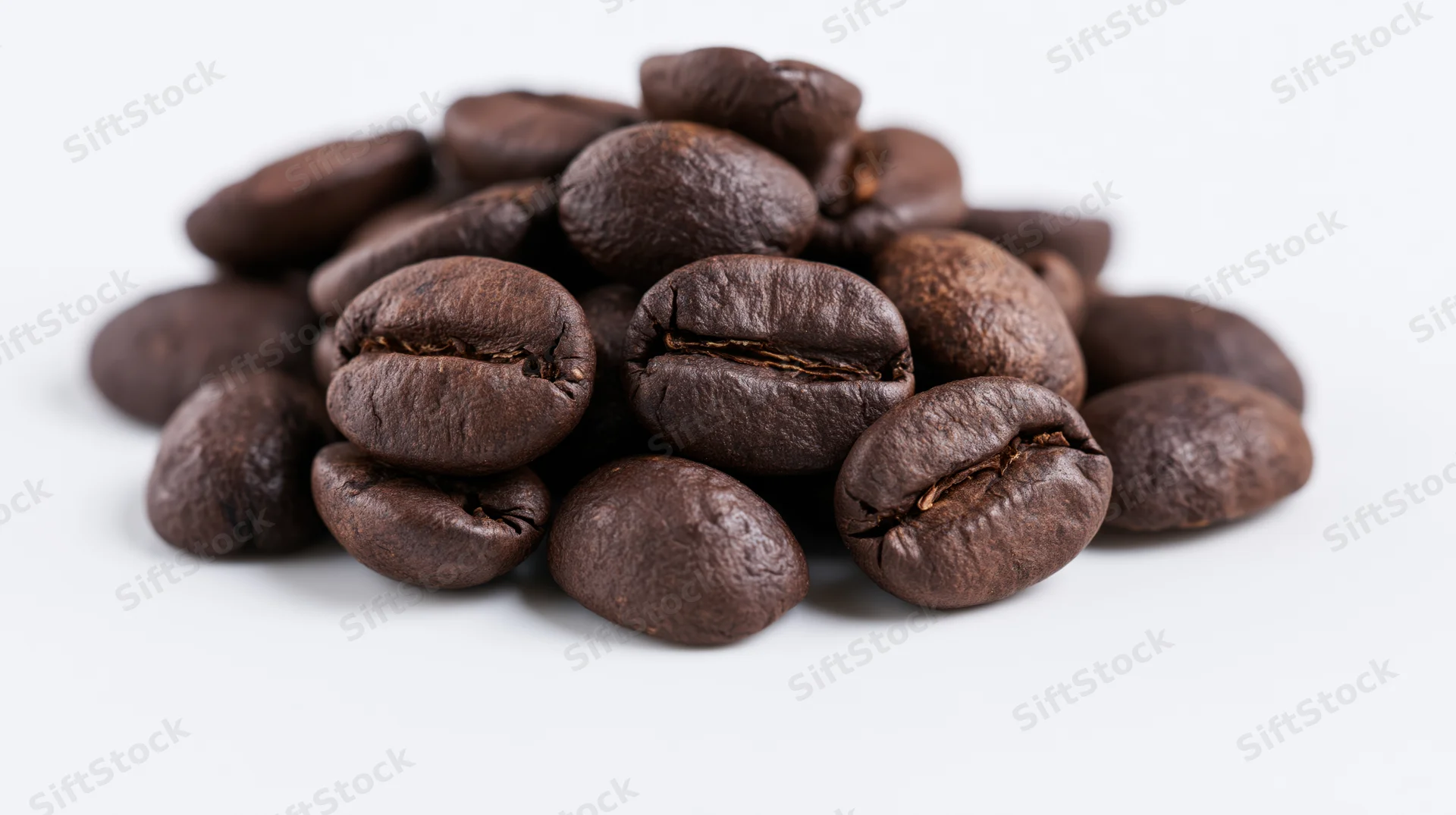 Dark roasted coffee beans piled loosely on a white surface