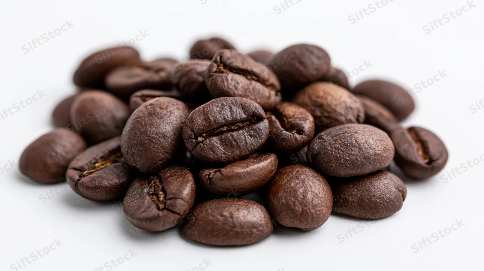 A small loose pile of dark roasted coffee beans on a white surface