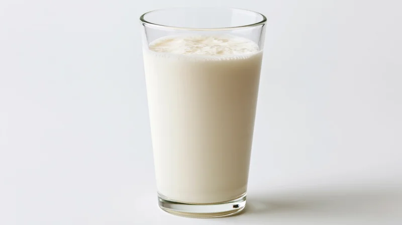 Tall clear glass filled with whole milk on white background
