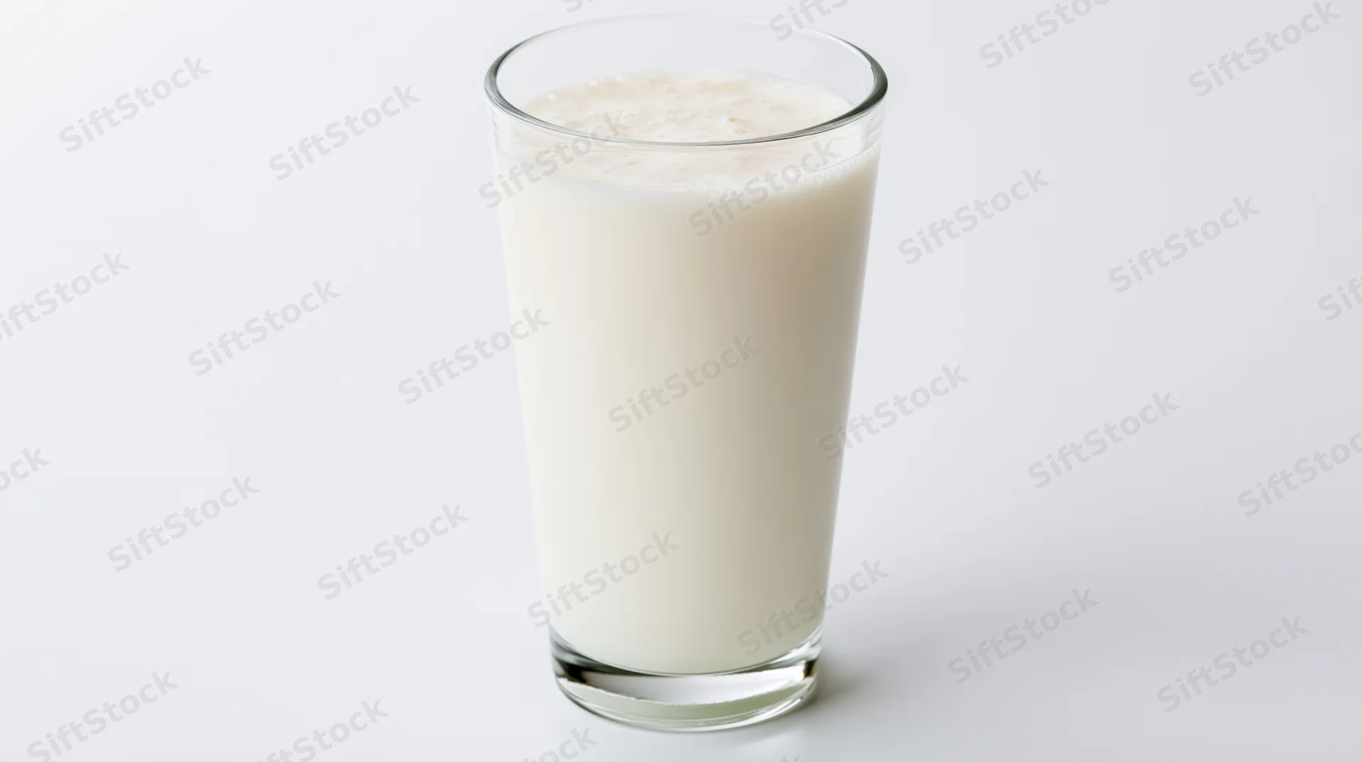 Tall clear glass filled with whole milk on white background