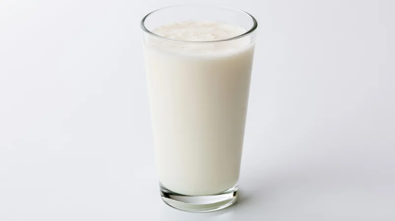 Tall clear glass filled with whole milk on white background