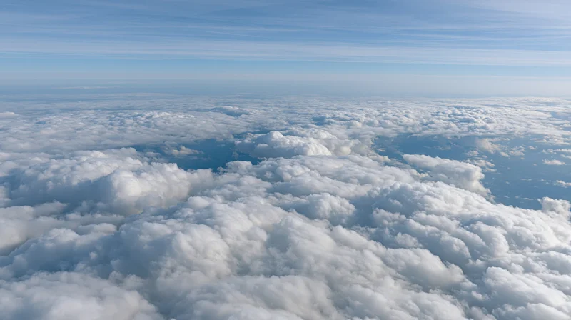 Aerial view above a dense layer of billowing cumulus clouds under a clear blue sky