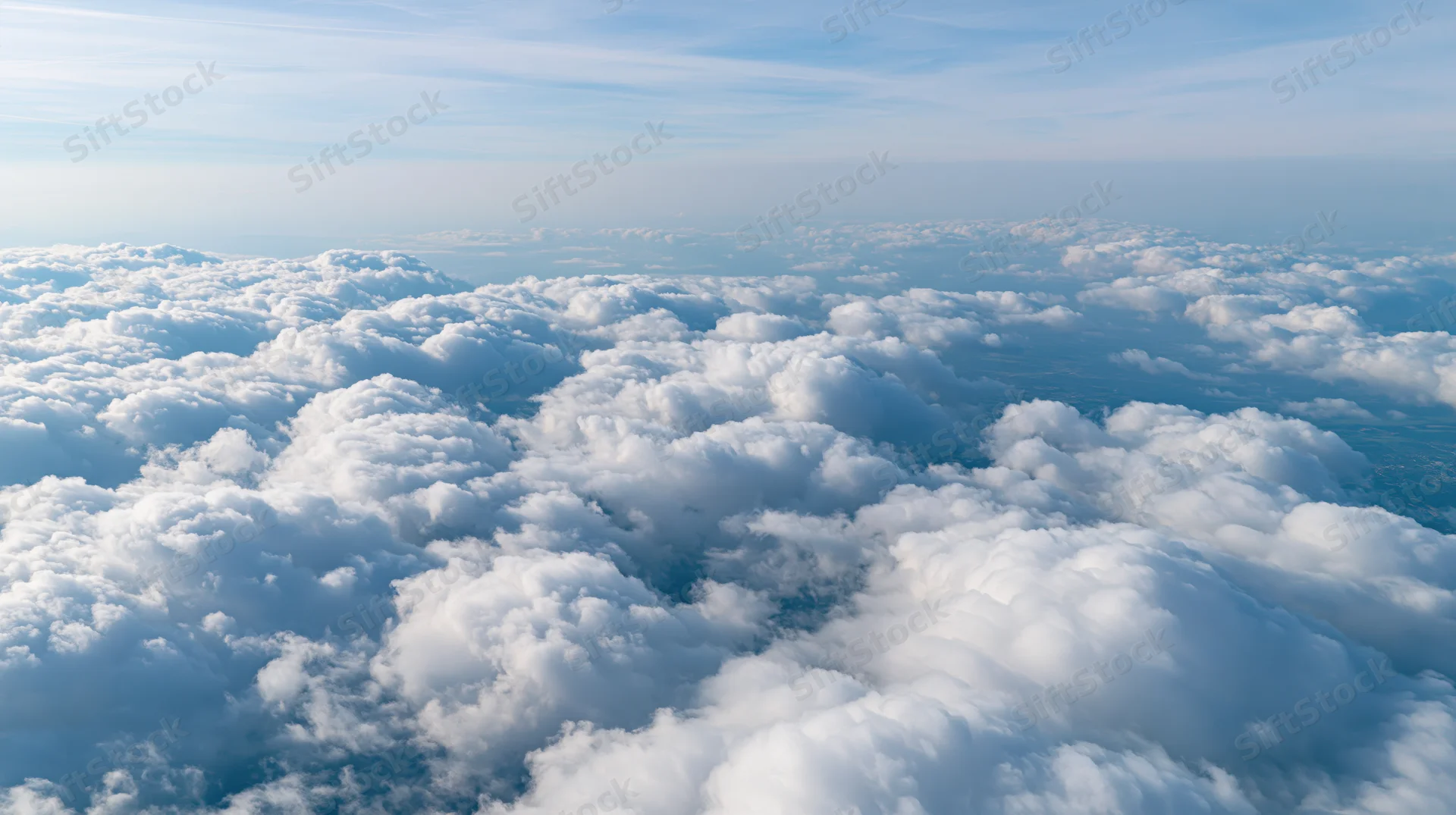 Aerial view above a dense layer of billowing cumulus clouds under a clear blue sky