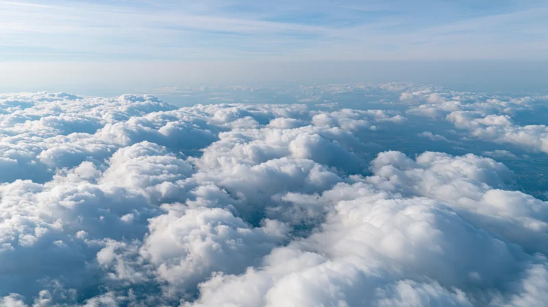 Aerial view above a dense layer of billowing cumulus clouds under a clear blue sky