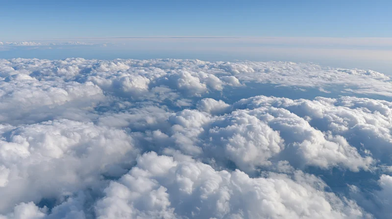 Aerial view above a dense layer of billowing cumulus clouds under clear blue sky