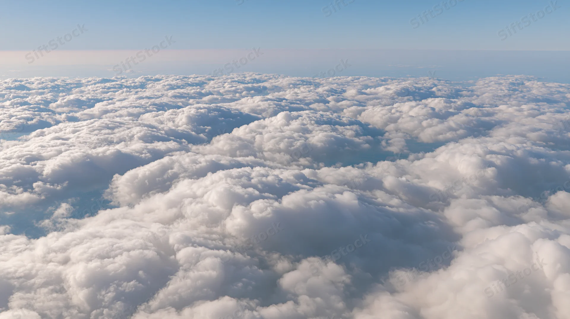 Aerial view above a dense layer of billowing cumulus clouds under a clear blue sky