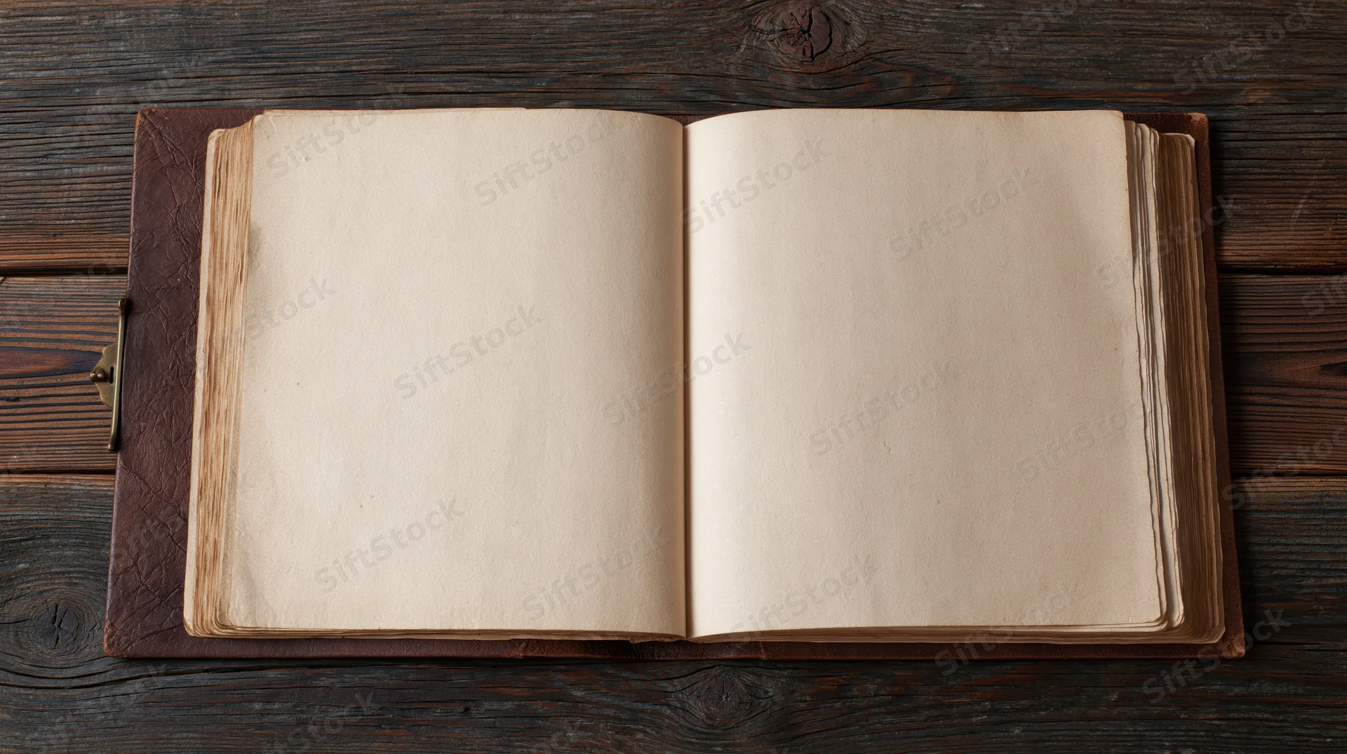 Open vintage leather-bound book with blank yellowed pages on dark wooden surface