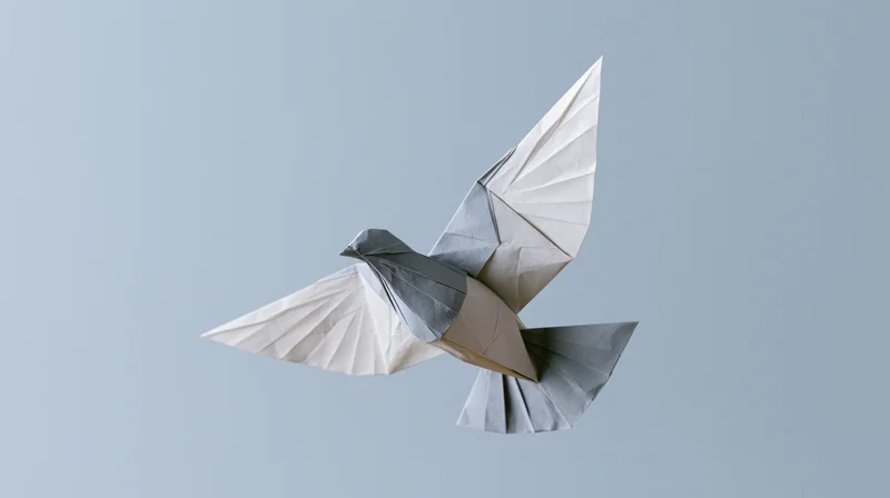 Origami dove in mid-flight with wings spread against a light gray background