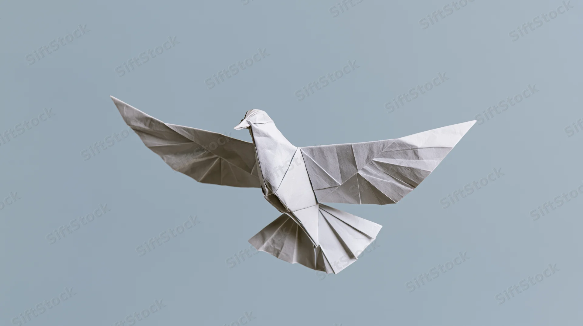 Origami paper dove with wings spread in midair against a light gray background