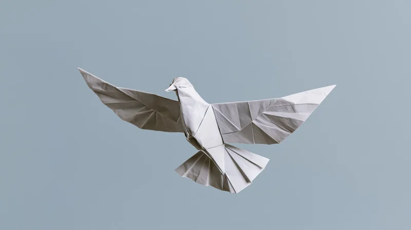 Origami paper dove with wings spread in midair against a light gray background