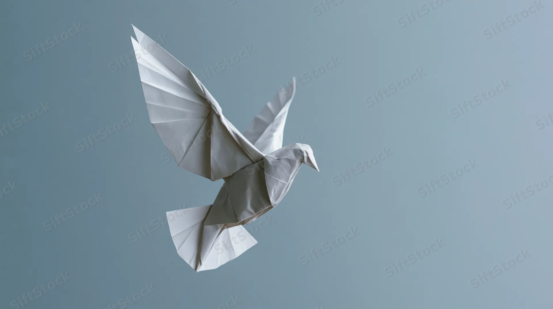 Origami paper dove in mid-flight with wings spread against a gray background