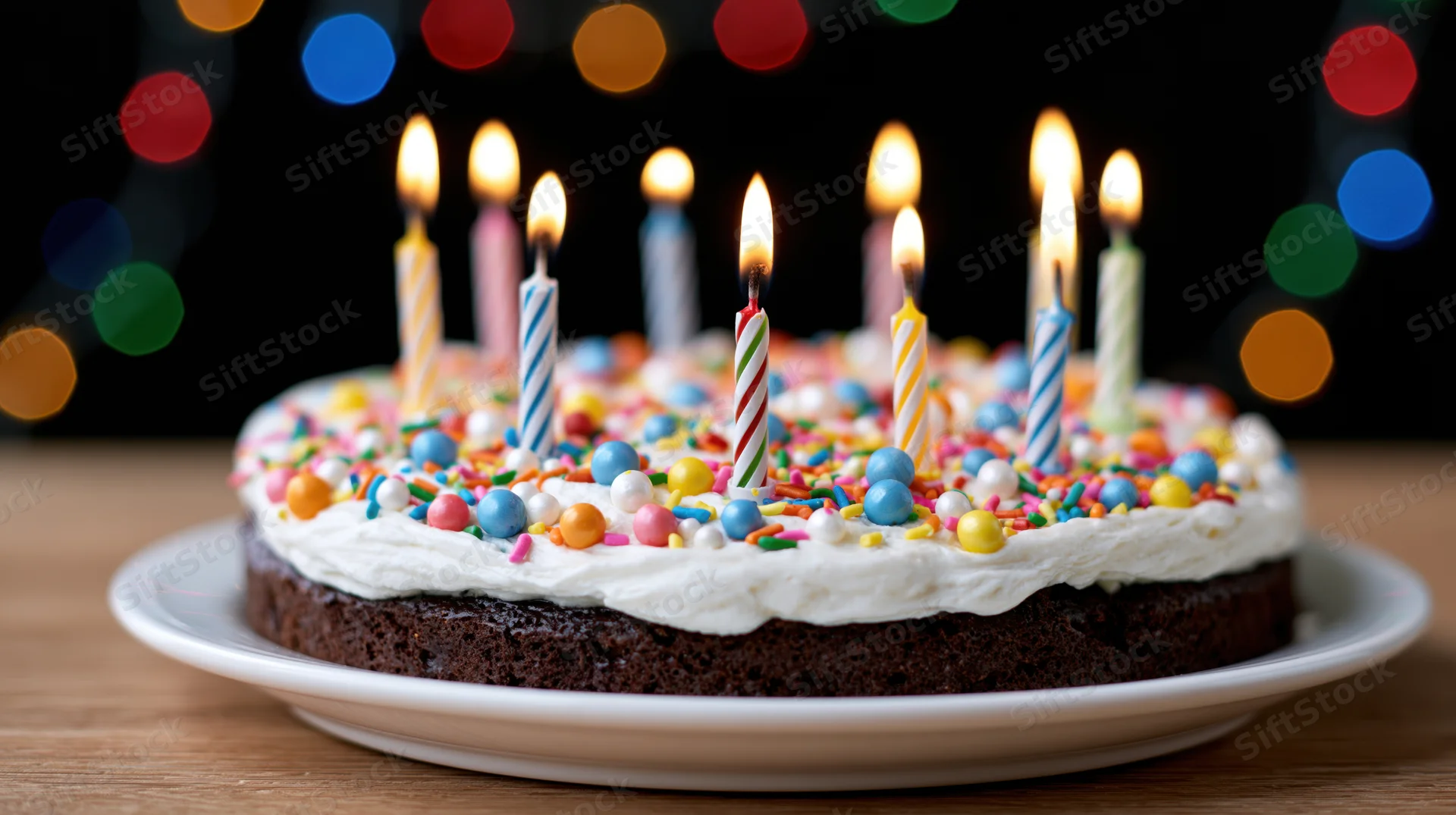 Chocolate birthday cake with lit striped candles and colorful sprinkles on a white plate