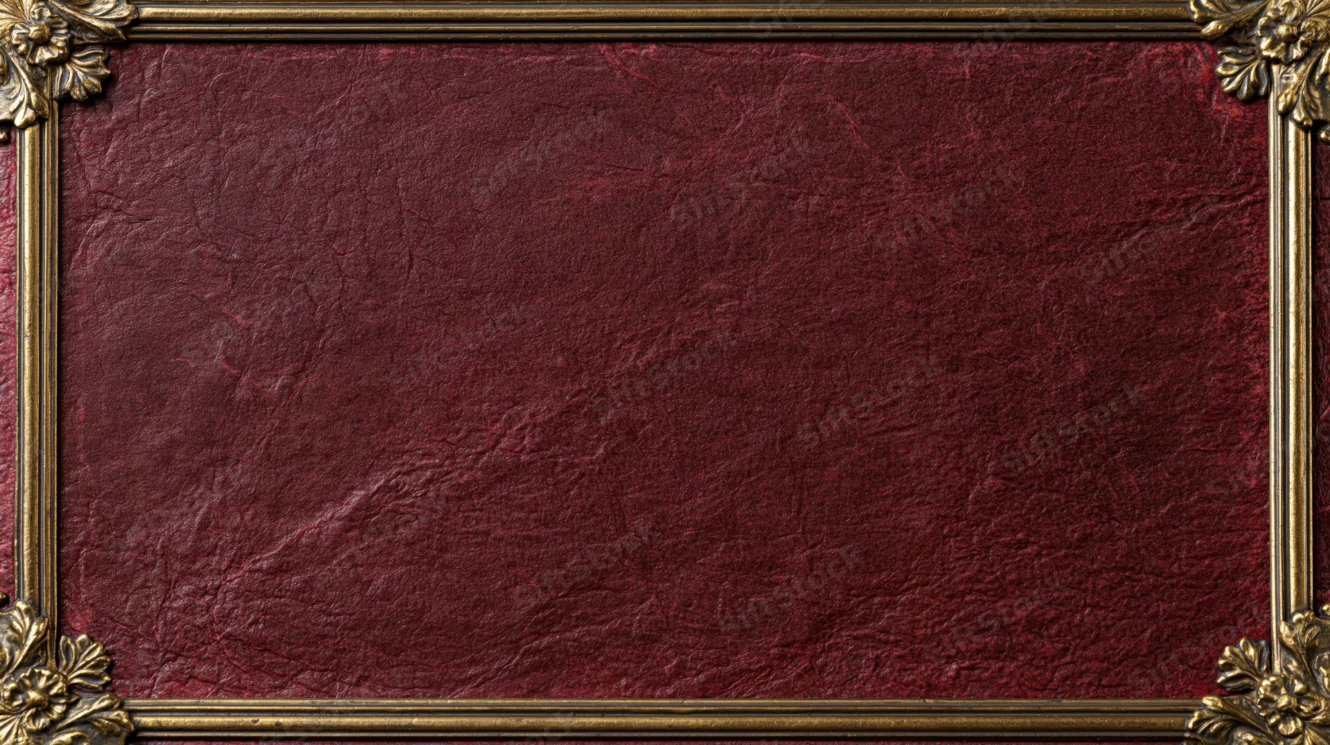 Close-up of an aged crimson leather book cover with ornate gold frame and floral corners