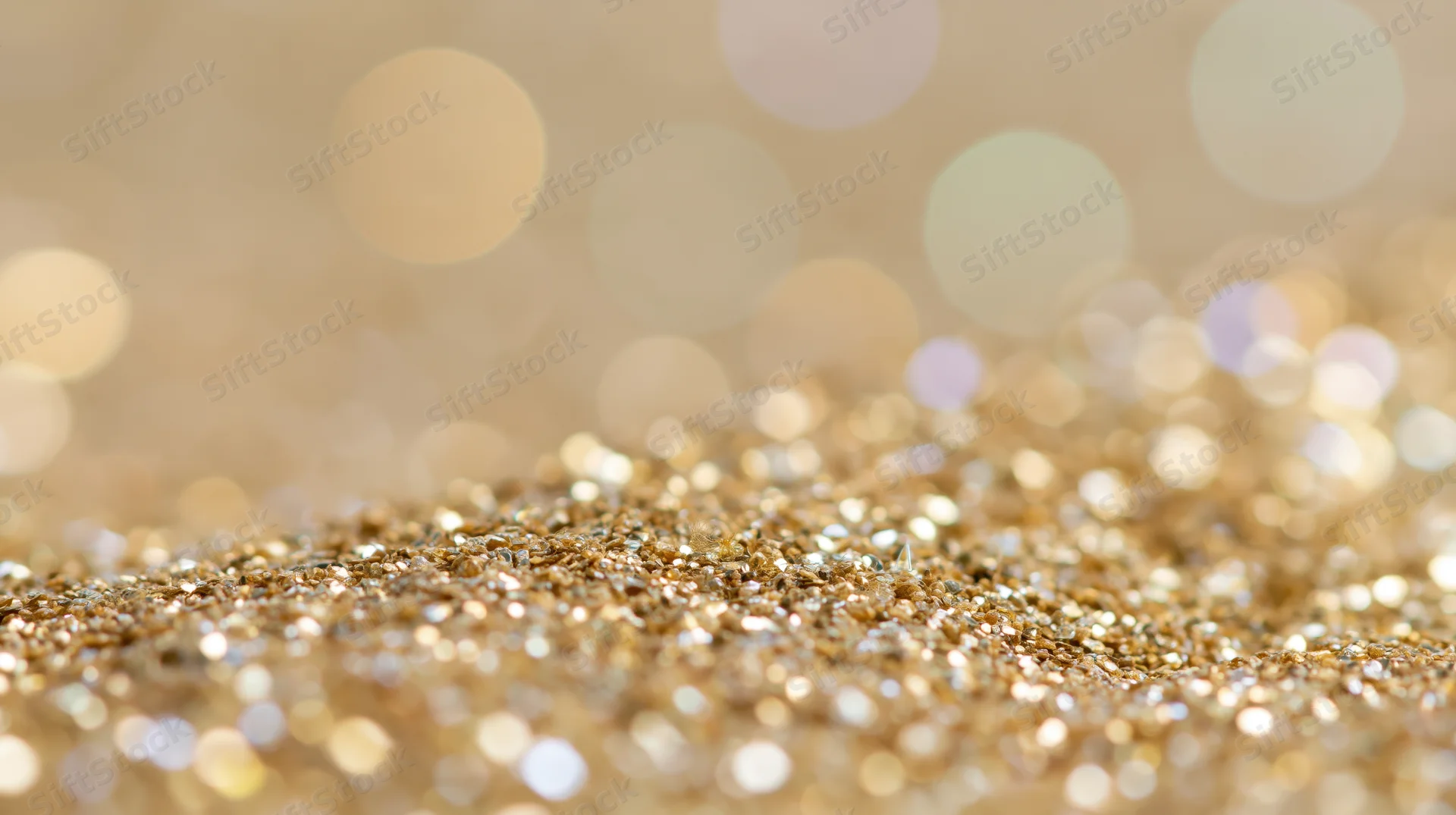 Close-up of gold glitter scattered across a surface with bokeh lights in the background