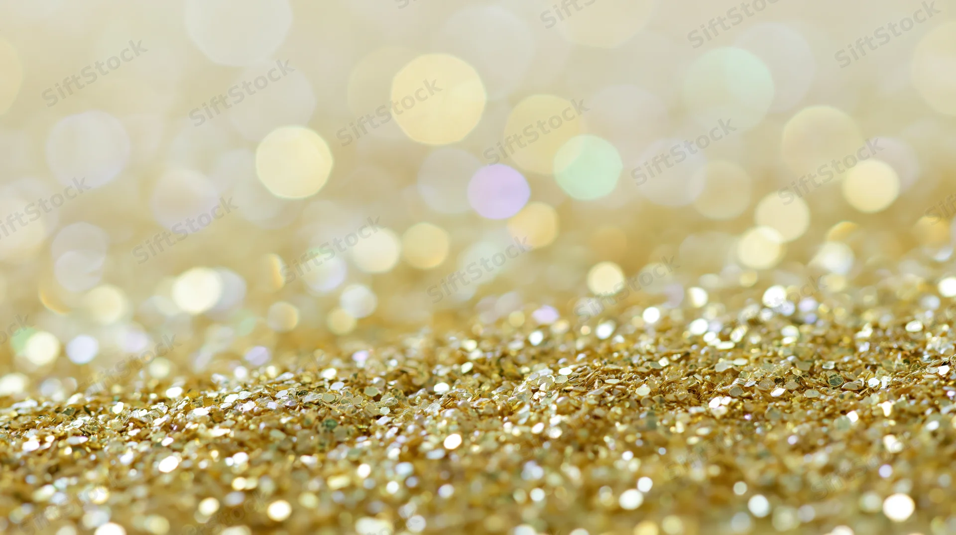 Close-up of gold glitter scattered across a surface with bokeh lights in the background