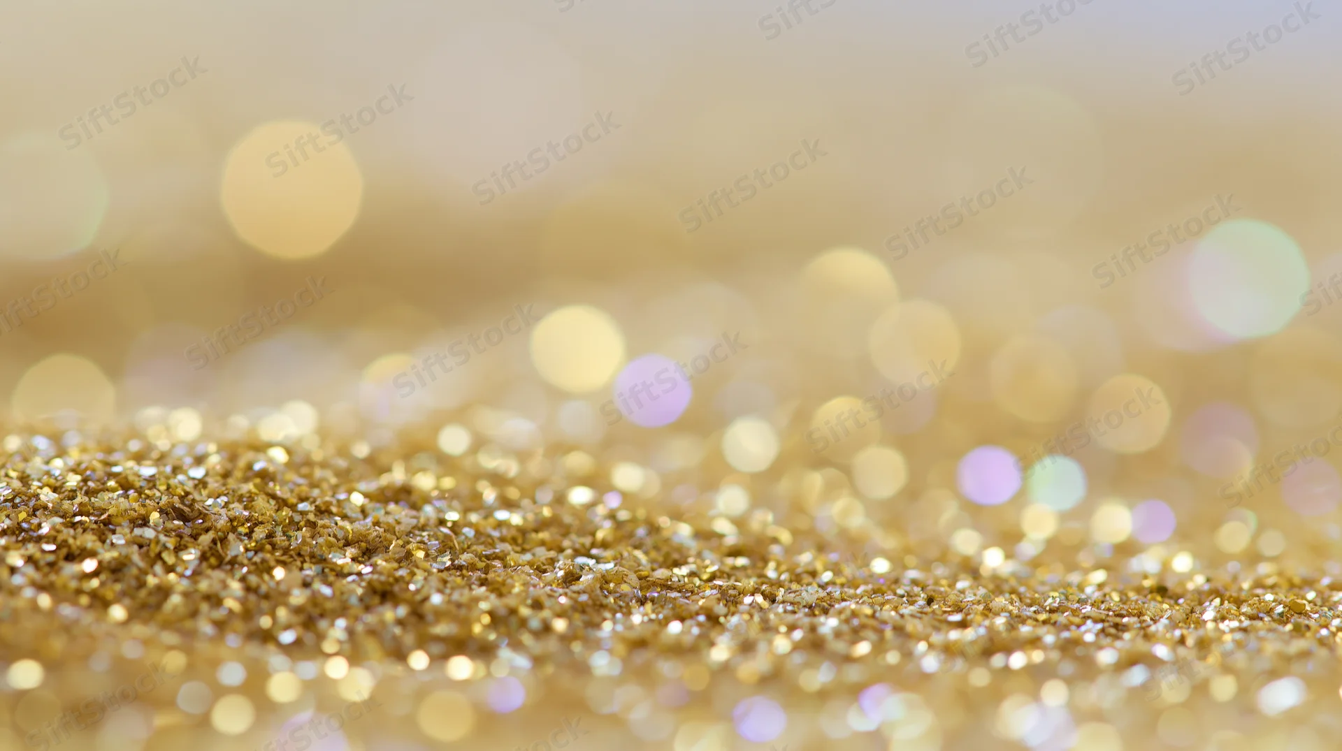Close-up of gold glitter scattered across a surface with bokeh lights in the background