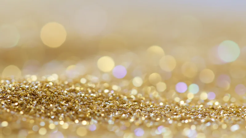 Close-up of gold glitter scattered across a surface with bokeh lights in the background