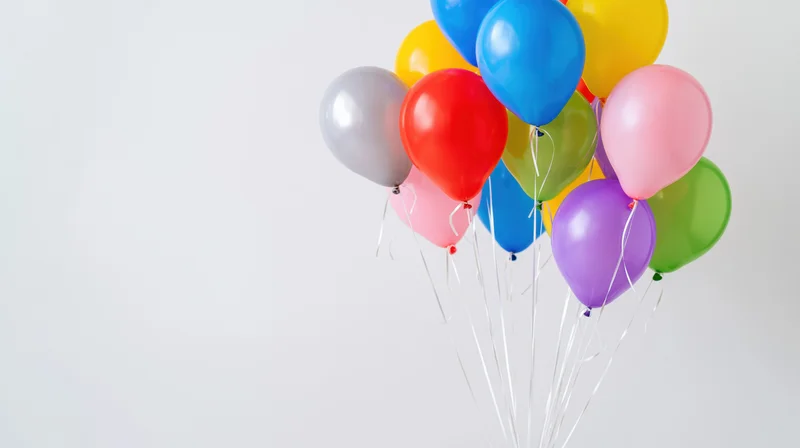 Cluster of colorful helium balloons floating against a white background with copyspace