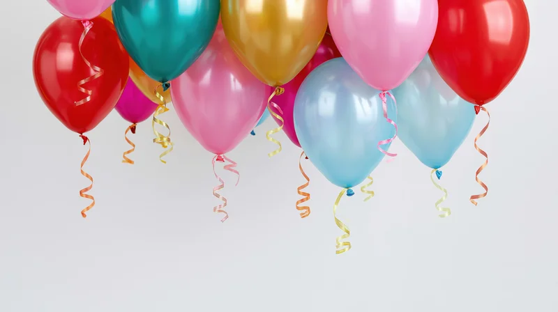 Cluster of colorful helium balloons floating near the top of a white background with copyspace below