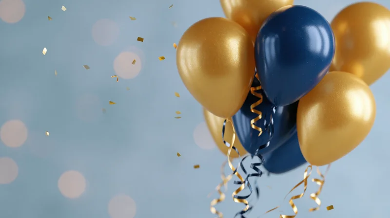 Cluster of gold and navy blue helium balloons floating with confetti and streamers against a soft blue background