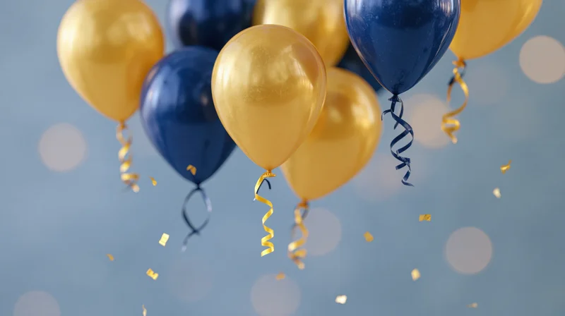 Gold and navy blue helium balloons floating with confetti and curling ribbons against a soft blue bokeh background