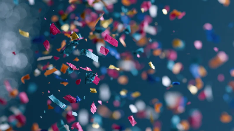 Colorful confetti pieces falling in mid-air against a dark blue background with bokeh lights