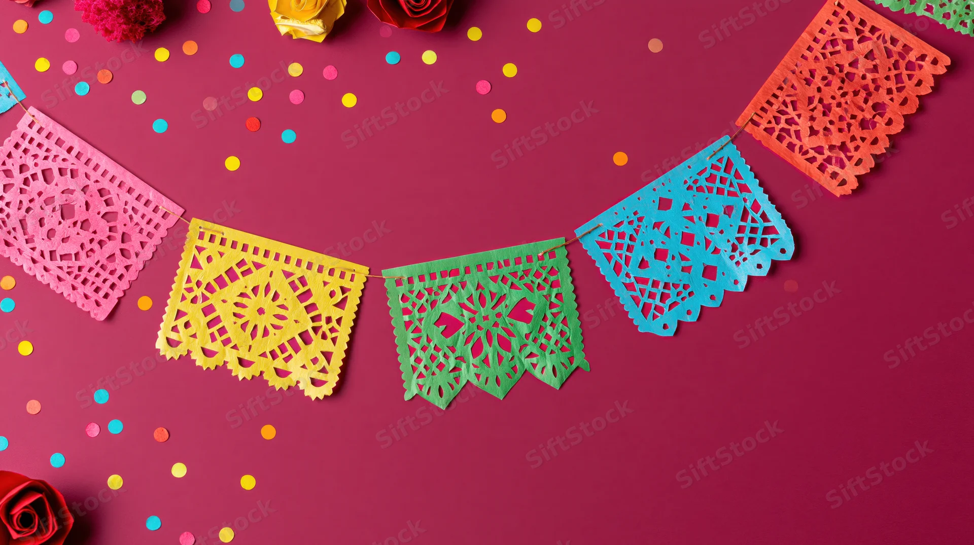 Colorful papel picado banner flags strung in an arc against a red background with confetti and roses